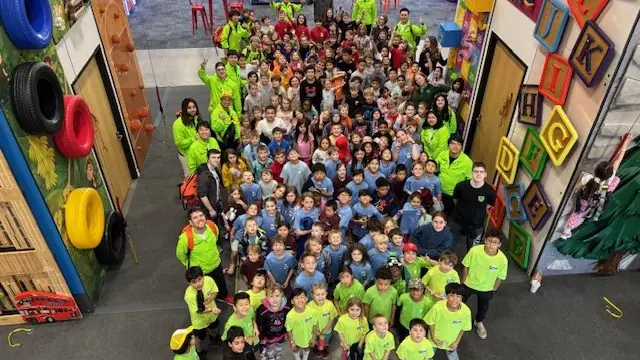 A full group posing in front of the climbing walls at UP!