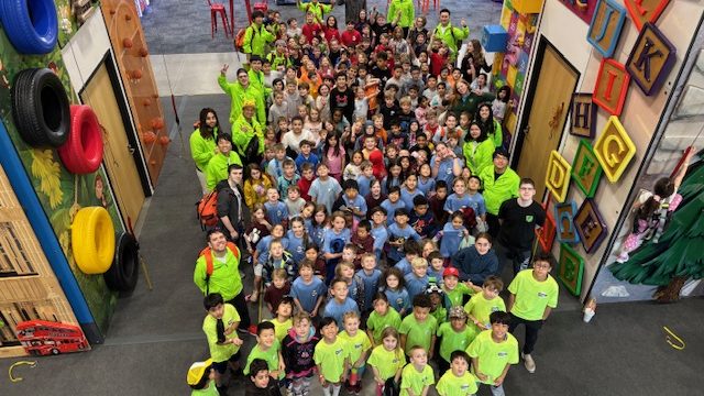 A full group posing in front of the climbing walls at UP!